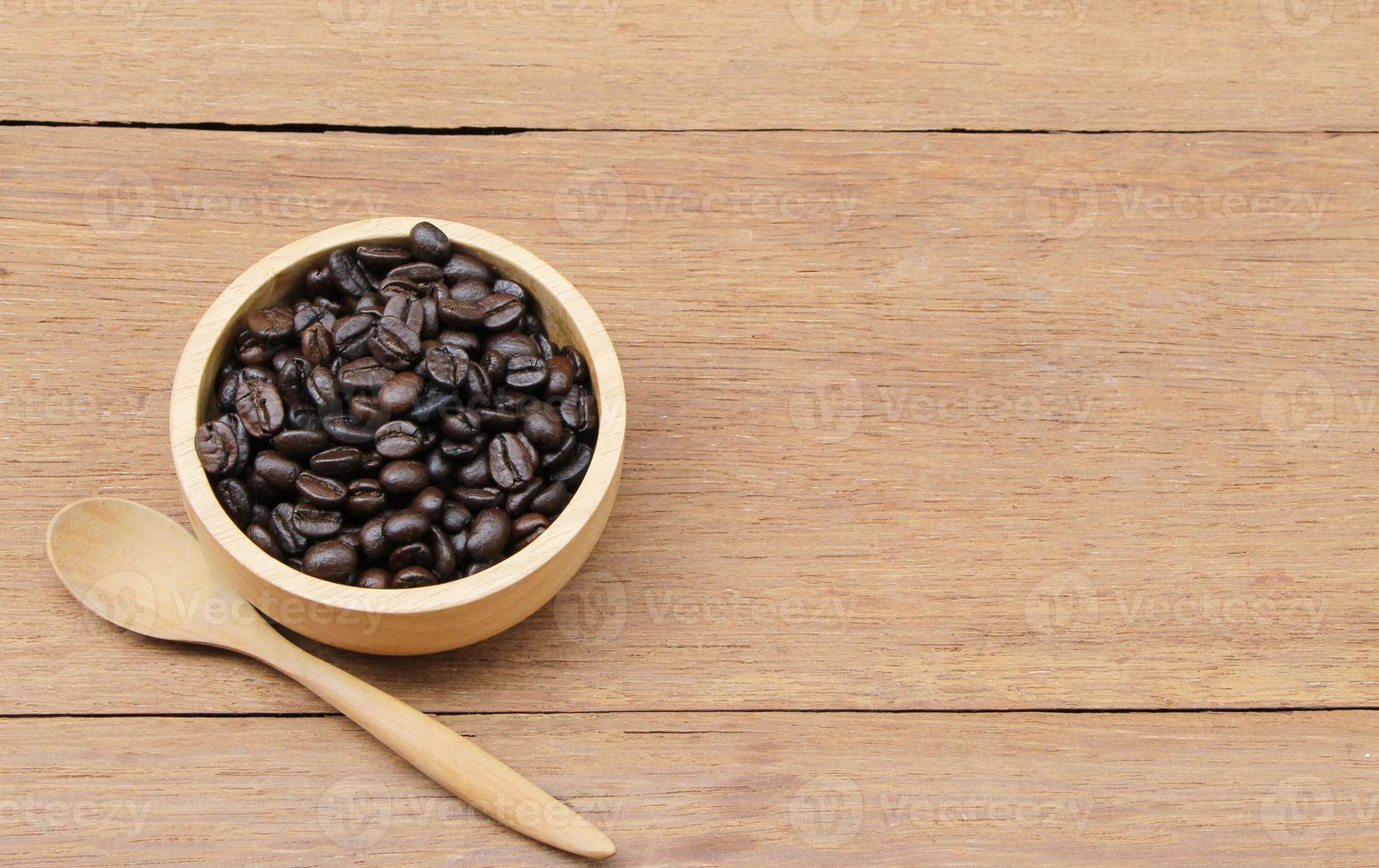 granos de café tostados en un cuenco de madera sobre una mesa rústica de madera con una cuchara. enfoque selectivo en los granos de café en un tazón foto