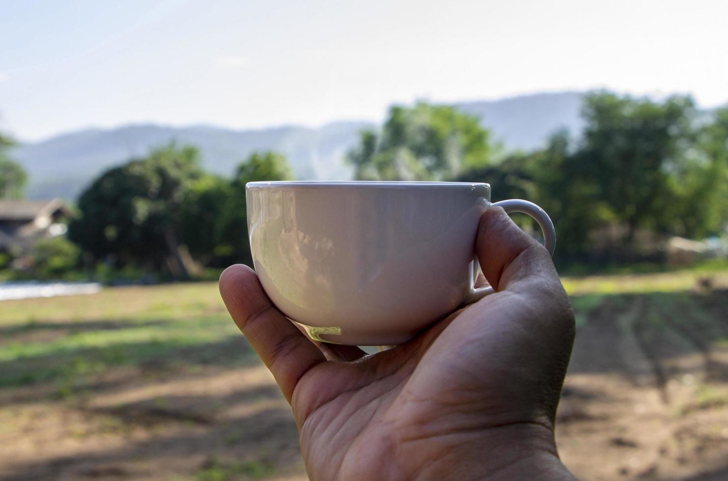 Bebidas refrescantes matutinas creativas concepto de una mano de hombre sosteniendo una taza de café con tierras de cultivo en un campo de fondo de Tailandia foto