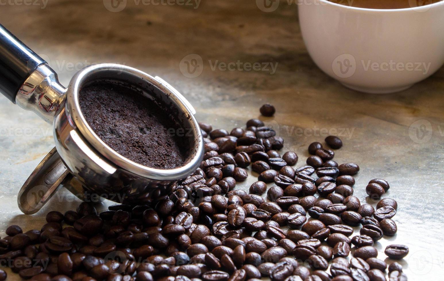 coffee grounds in a filter basket after extraction with a pile of organic arabica coffee beans on a concrete table. Focus on a filter basket photo