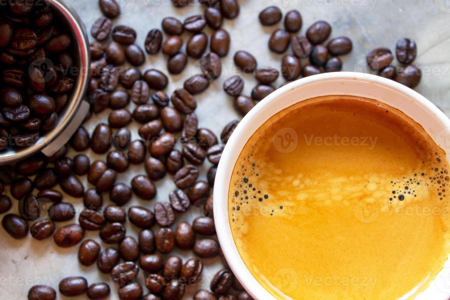 vista superior de una taza de café americano con una bonita crema en la parte superior sobre una mesa de hormigón con un montón de granos de café arábica orgánicos y una cesta portafiltros cerca. foto