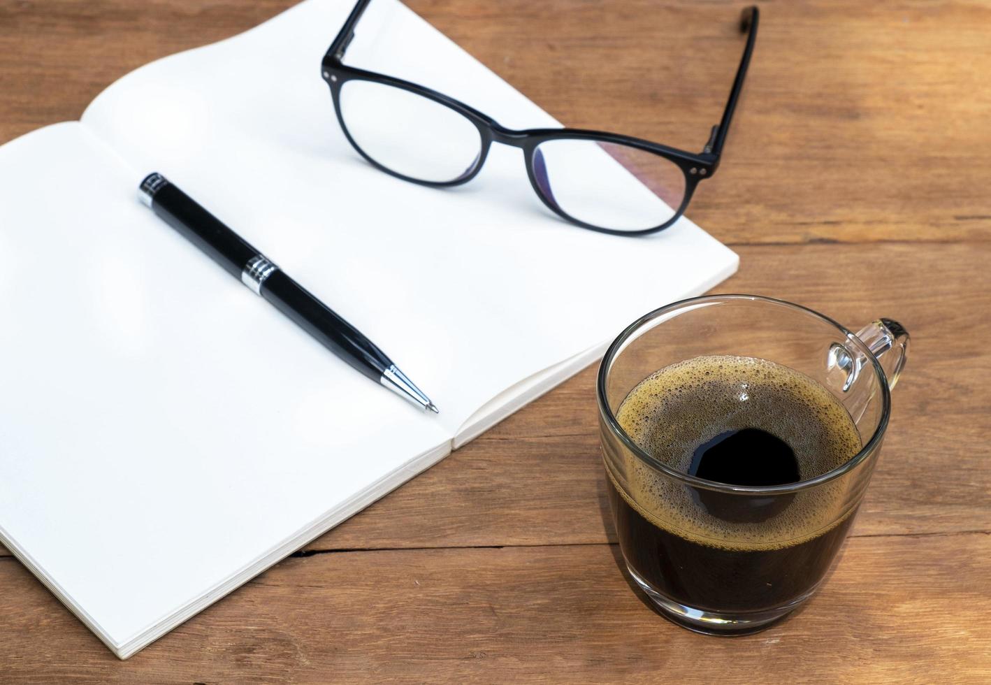 cup of coffee on a wooden table with notebook and pen photo