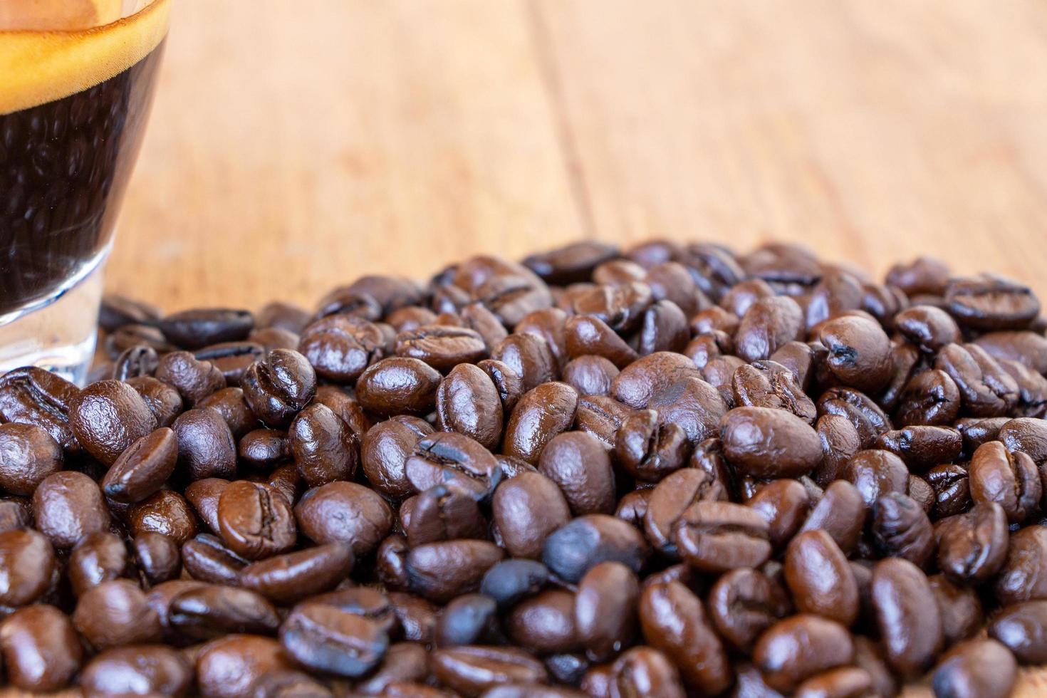 Cierra el montón de granos de café orgánicos tostados de color marrón oscuro sobre una mesa de madera. enfoque selectivo en medio del montón de granos de café foto