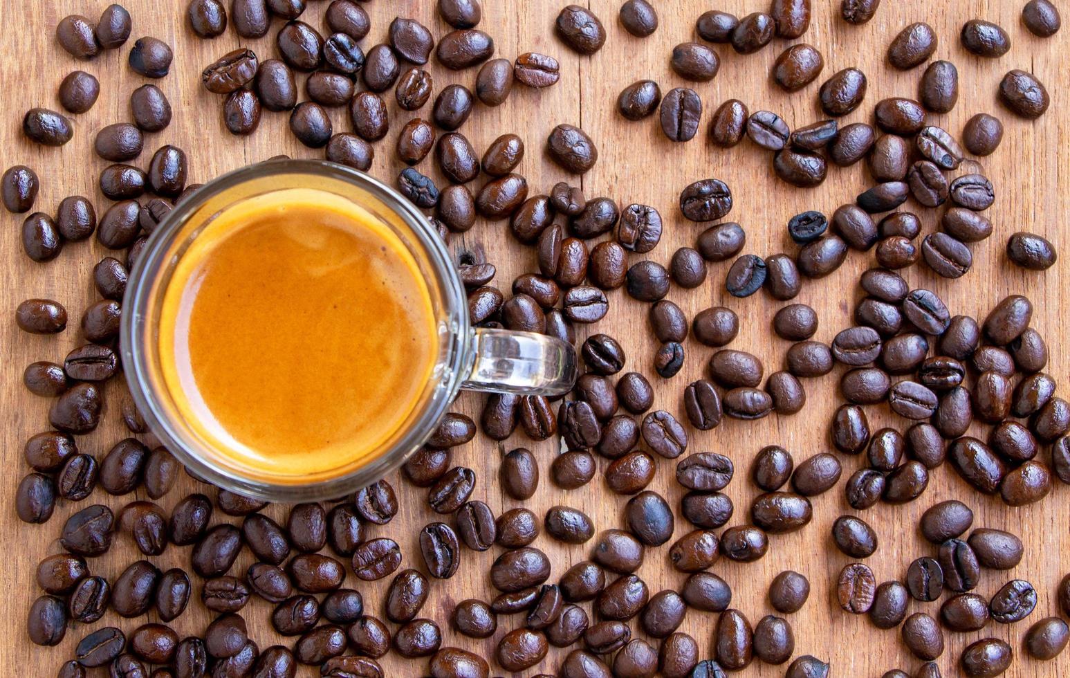 top view of a cup of hot espresso coffee with a nice crema on a wooden table with roasted coffee beans scattering around. Focus on a cup of coffee photo