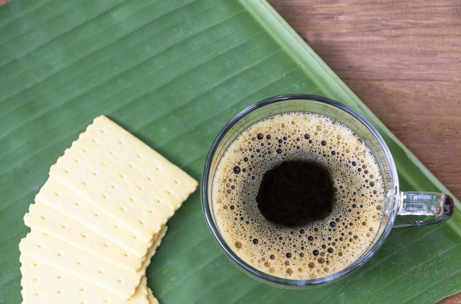 vista superior de un café negro en una taza sobre una hoja de plátano y una mesa de madera. foto