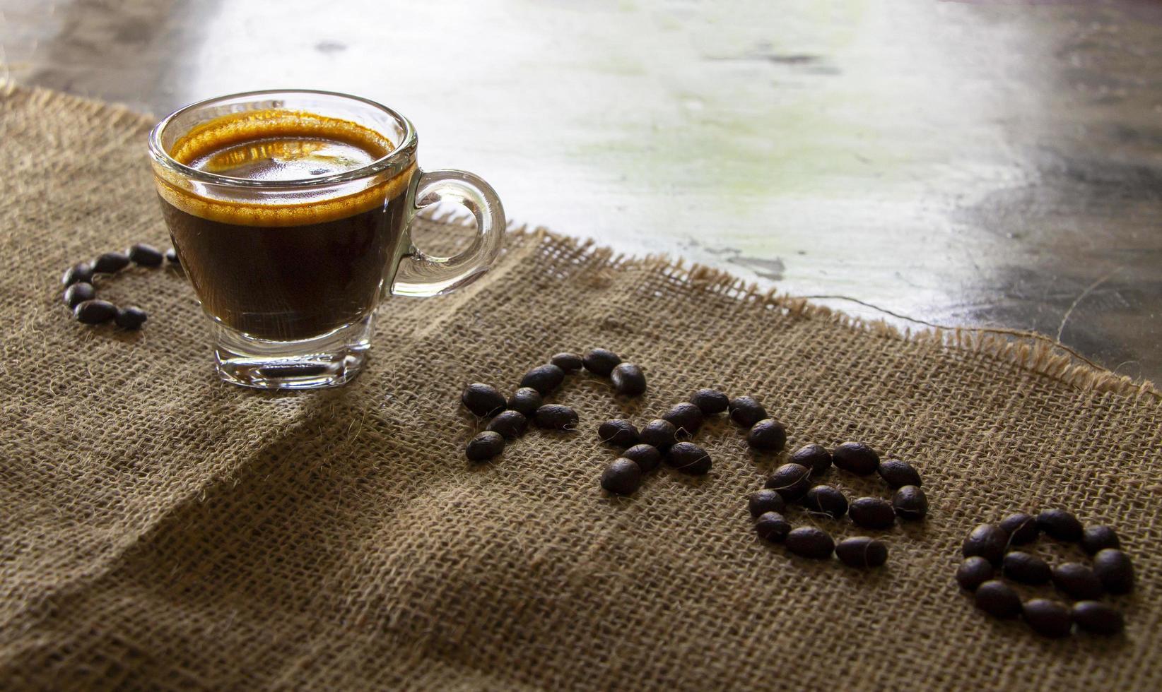 vista en ángulo alto de una taza de café espresso negro con una bonita crema sobre tela de saco y café arábica marrón. luz solar natural. refrescarse con una bebida caliente en un concepto matutino foto