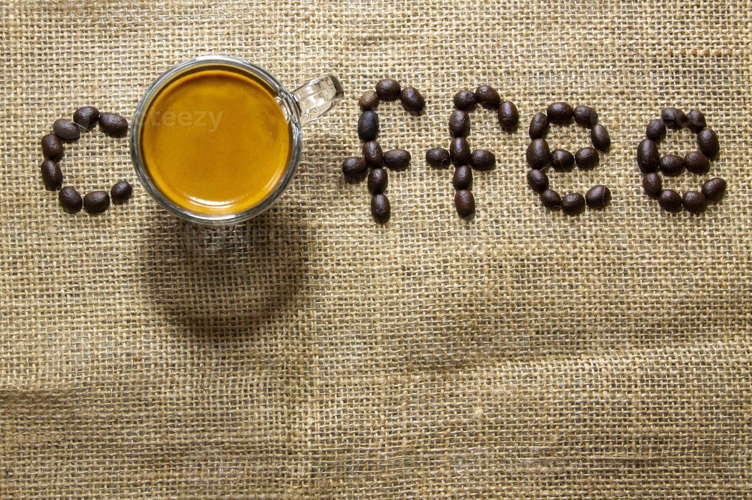 top view of a cup of black espresso coffee with a nice crema on sackcloth and brown arabica coffee bean. Natural sunlight, refresh by a good drink with caffeine photo