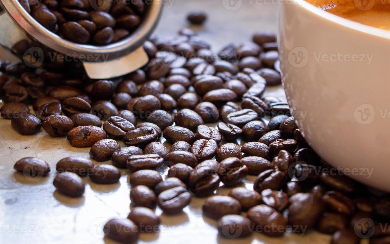 organic roasted arabica coffee beans on a concrete table between the basket of the filter holder and coffee cup. Focus on coffee beans in the middle of the pile photo