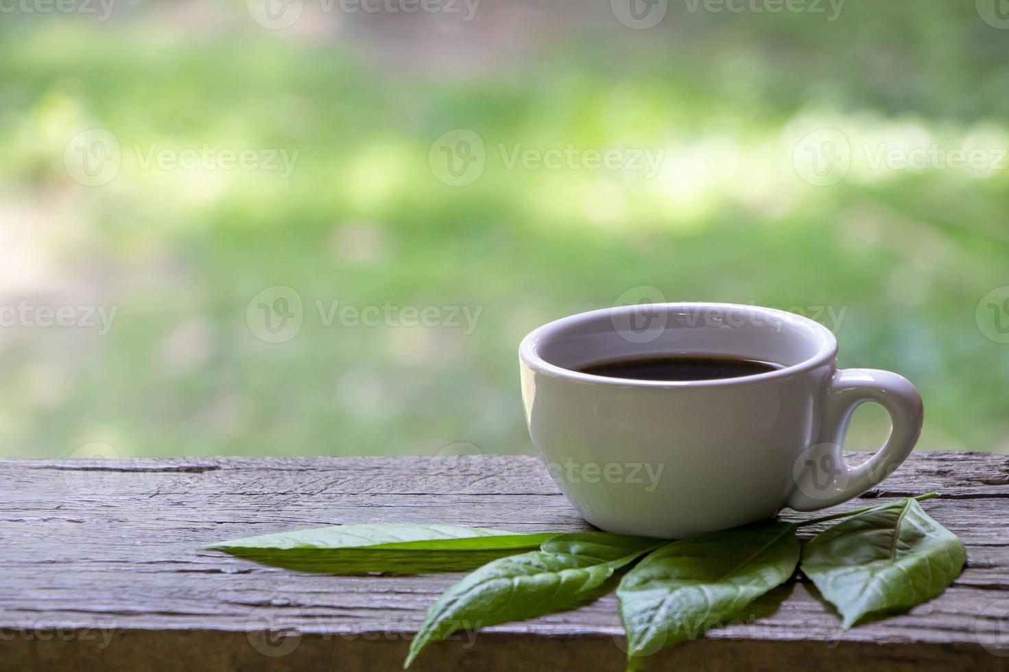 taza blanca de café negro sobre una mesa de madera de fondo natural. foto