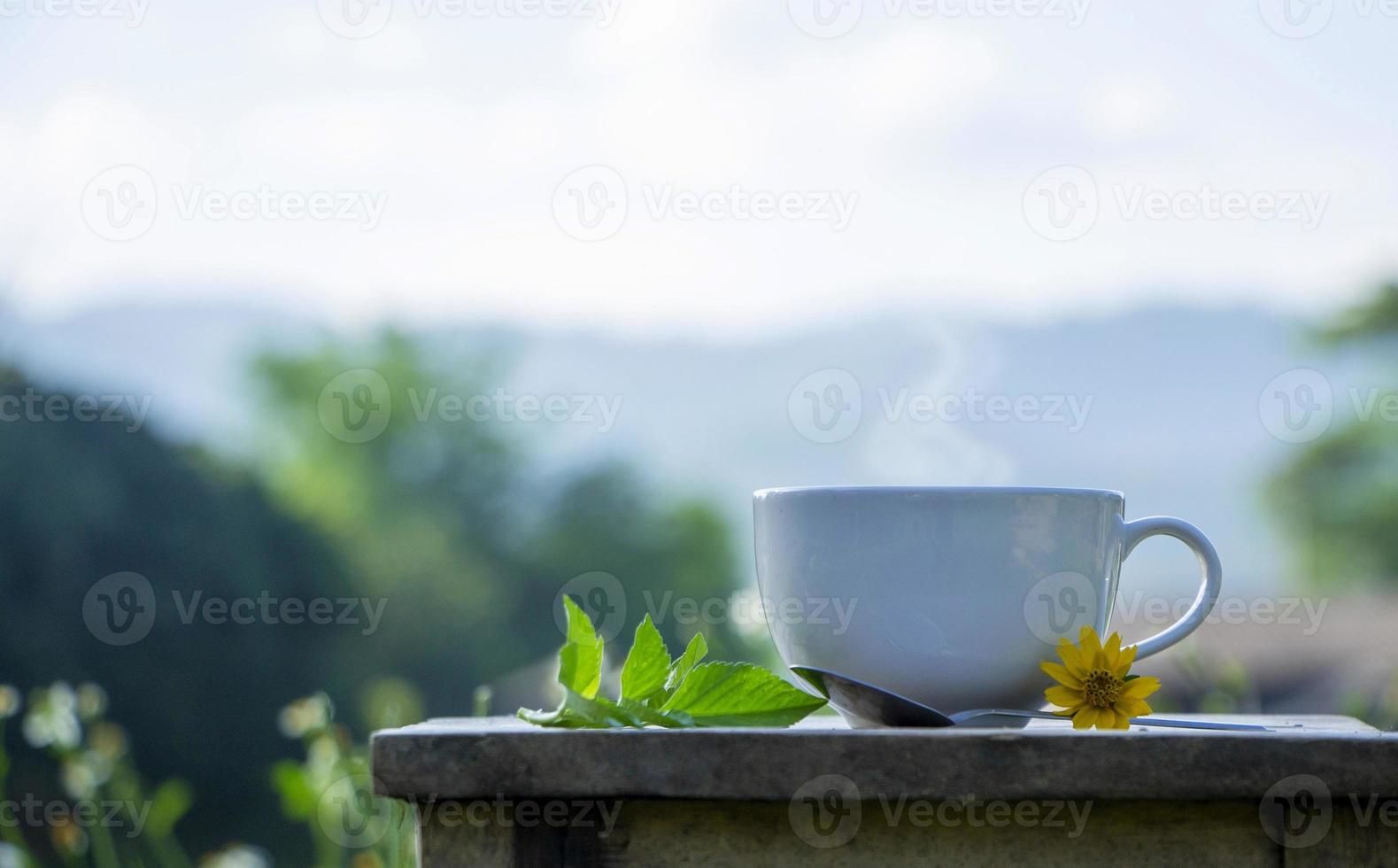 front view of a white ceramic cup of hot coffee on a rustic wooden table in natural background. Morning refreshment and drinks concept photo