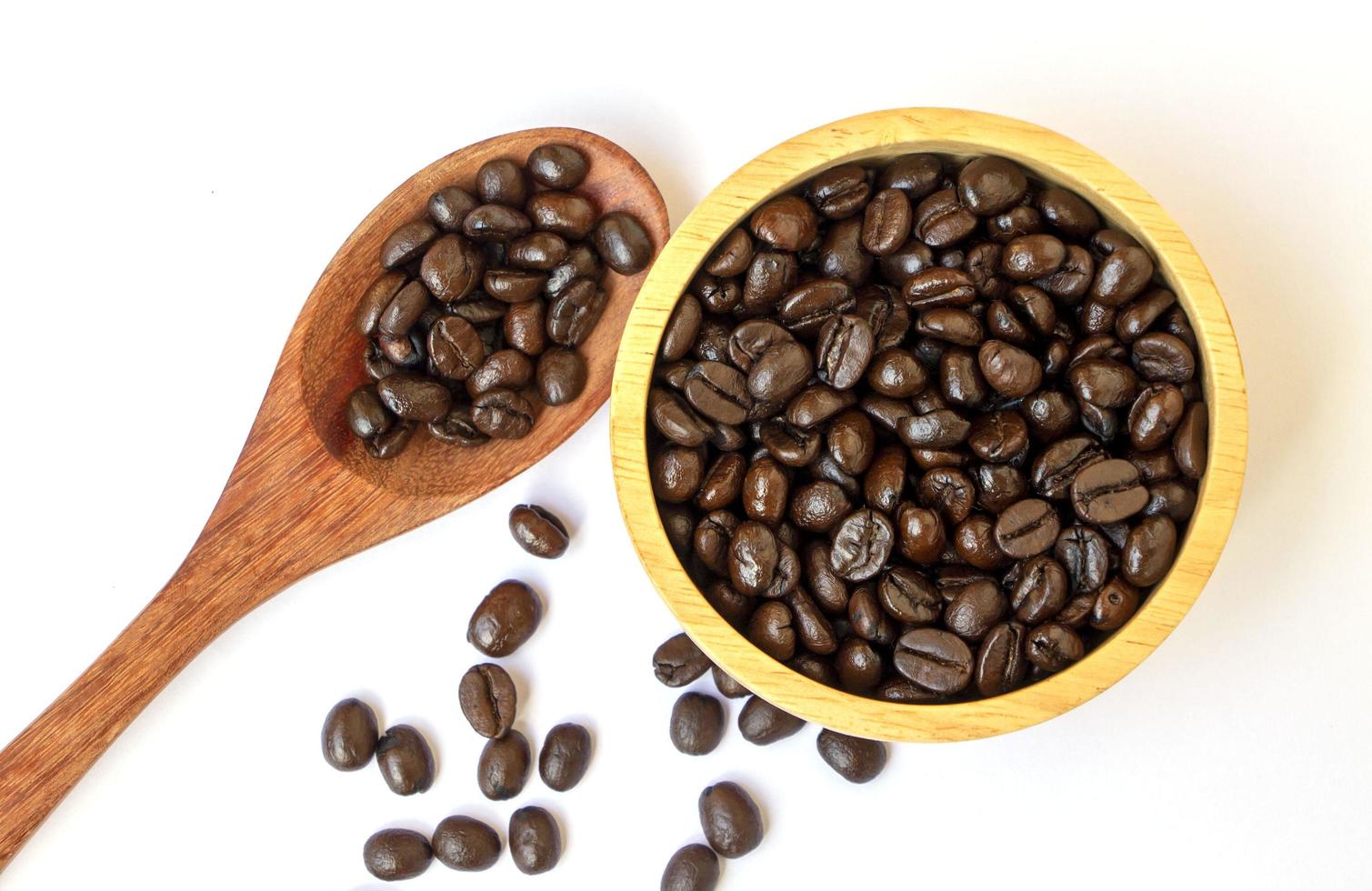 granos de café arábica tostados orgánicos en un tazón de madera y una cuchara sobre fondo blanco. concéntrese en los granos de café en un tazón. grano de café famoso y de buena calidad de chiangmai, tailandia foto