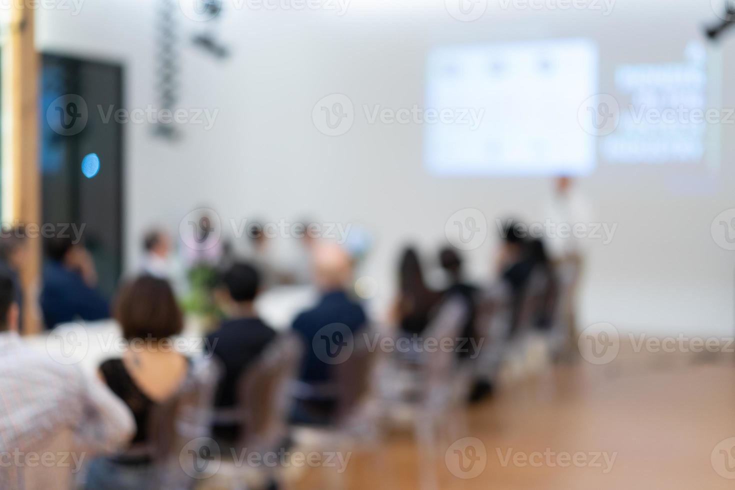 Blurry business presentation with the projector and white screen to the Asian audiences sit in the long table line. photo