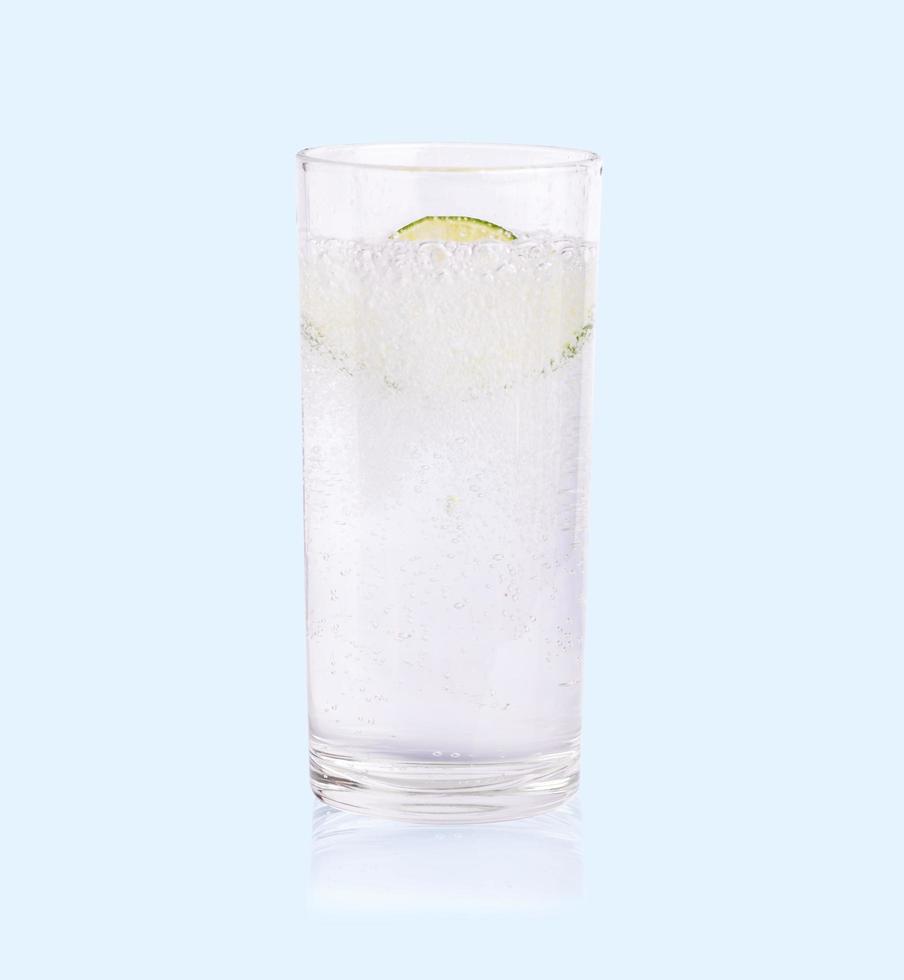 Green lime sliced falling in the soda water of glass on the soft blue background photo