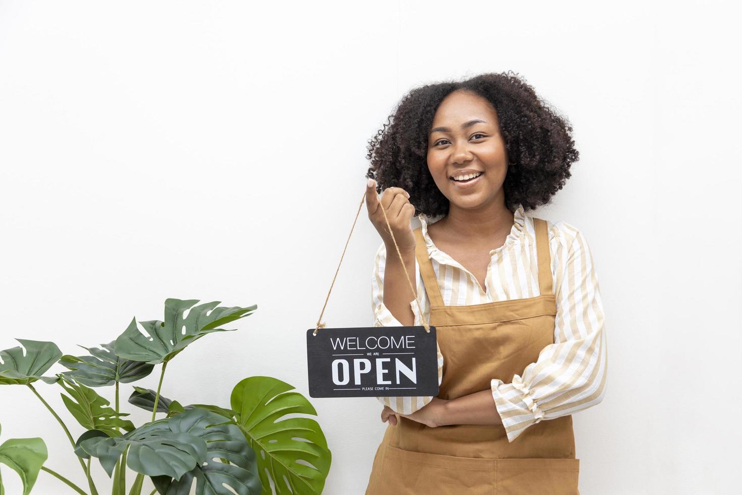 African American barista with apron is holding open sign in front of the coffee shop for cafe and small restaurant service concept photo