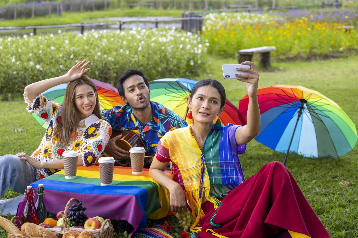 Group of transgender and homosexual people taking selfie and celebrating LGBTQ pride month in colorful dress and rainbow flag while picnic in the park photo