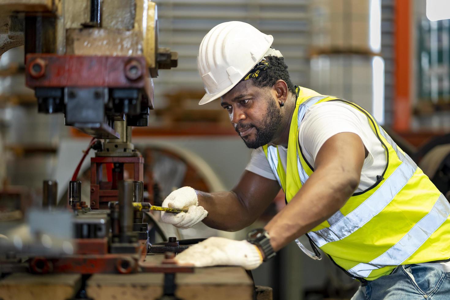 trabajador industrial afroamericano está utilizando una máquina de prensa hidráulica para fabricar piezas de metal y acero mientras trabaja dentro de la fábrica de techos galvanizados de chapa metálica para el concepto de la industria de seguridad foto