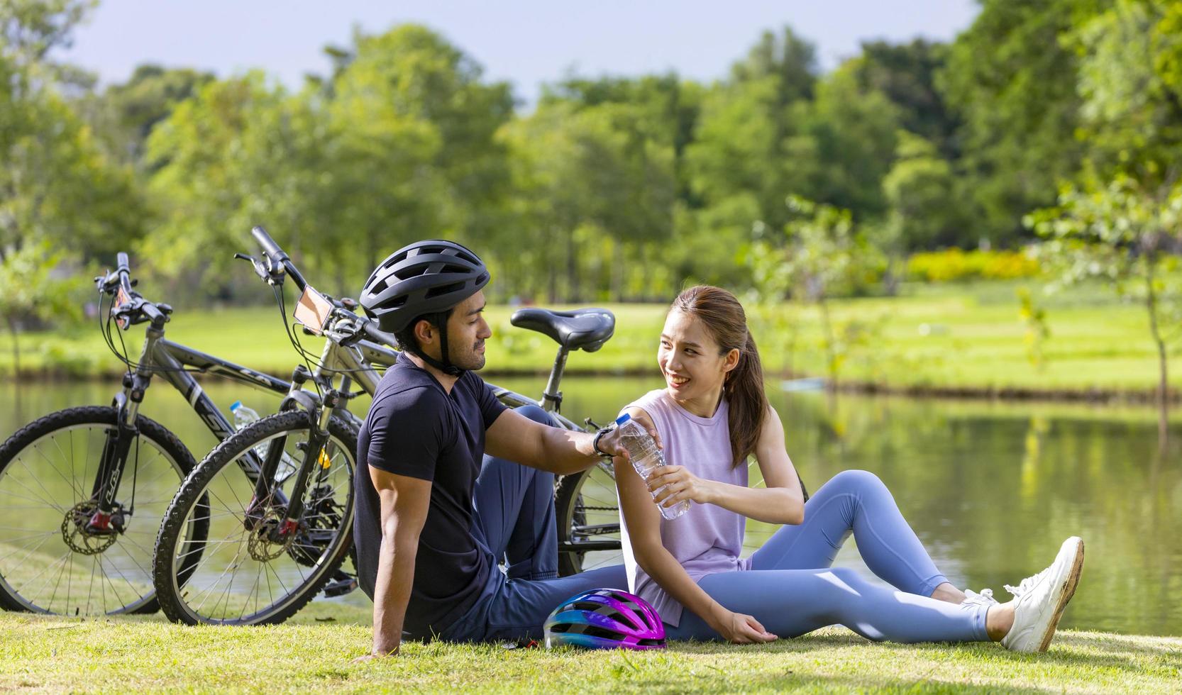 joven pareja asiática descansando después de andar en bicicleta en el parque público para actividades de ejercicio de fin de semana y concepto de búsqueda recreativa foto