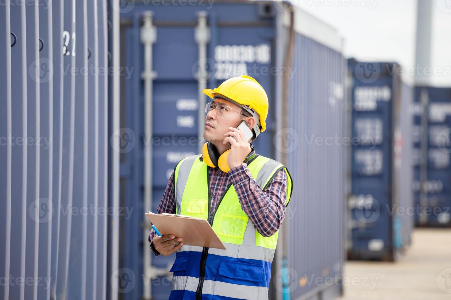 Engineer using smartphone with holding clipboard checklist in industry containers cargo, Foreman dock worker in hardhat and safety vest control loading containers box from cargo photo