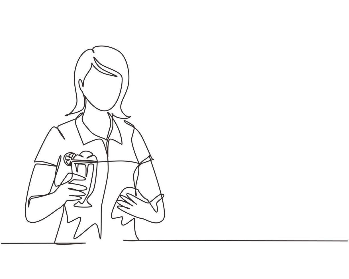 Single continuous line drawing young girl holding and showing glass of milkshake in office. Attractive lady having break at work and drink milkshake with slice of orange. One line draw design vector