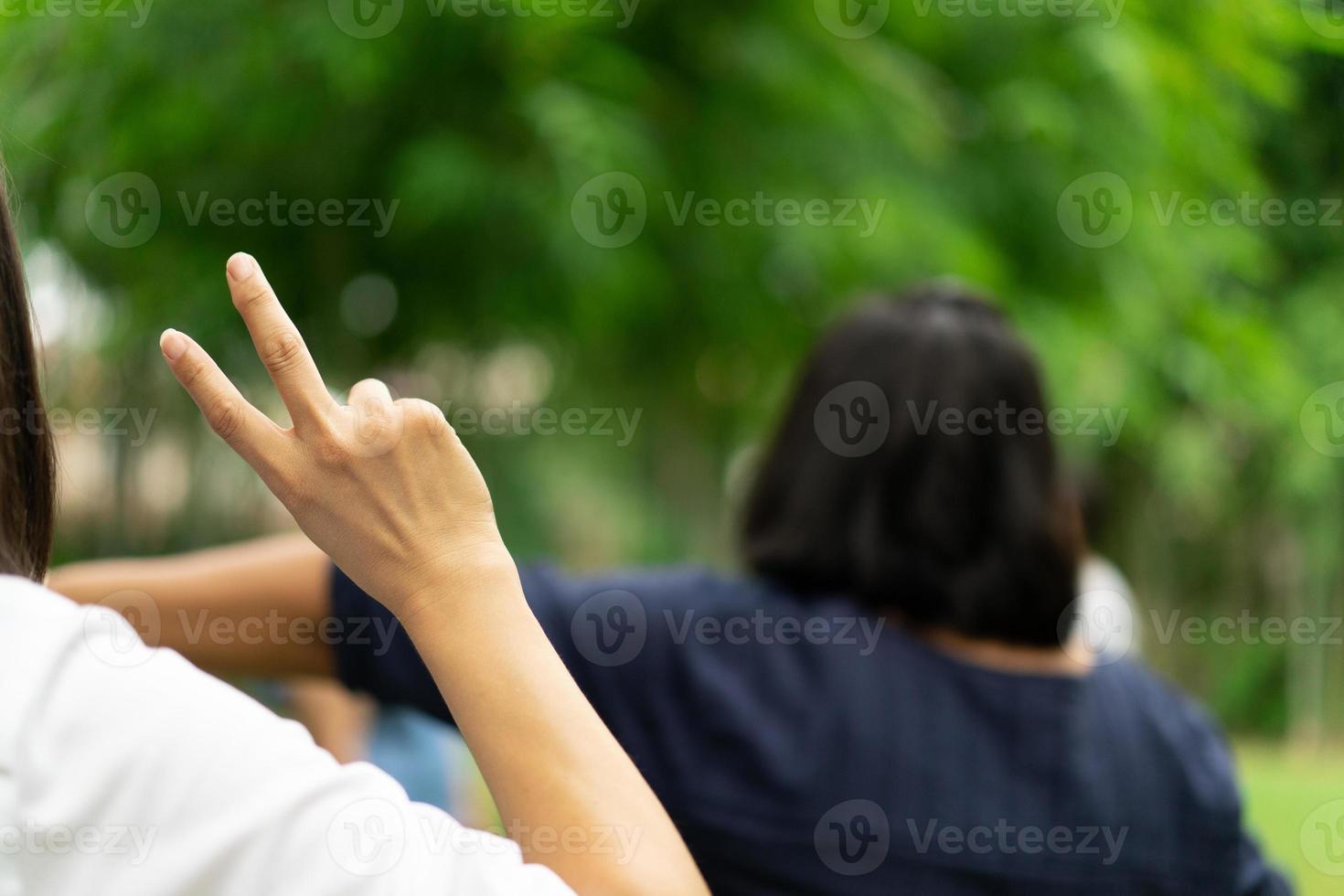 la mujer levanta la mano y muestra dos dedos de su mano en el jardín, desdibuja a otra gente en el fondo. foto