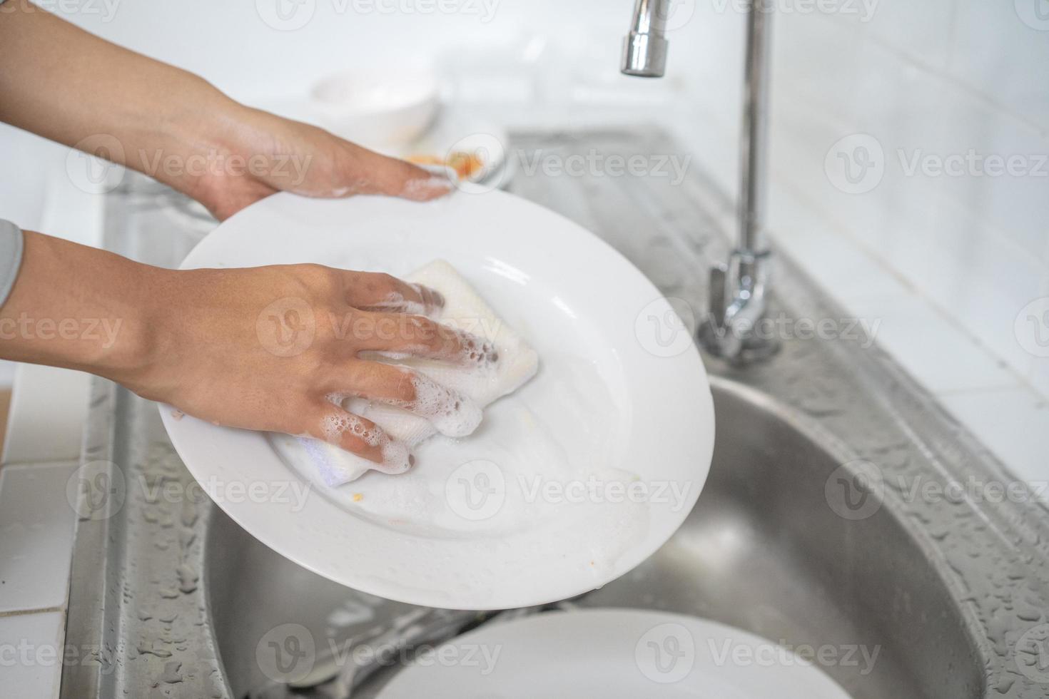 cerca de una mujer asiática lava el plato en la cocina con su esponja para lavar platos. foto