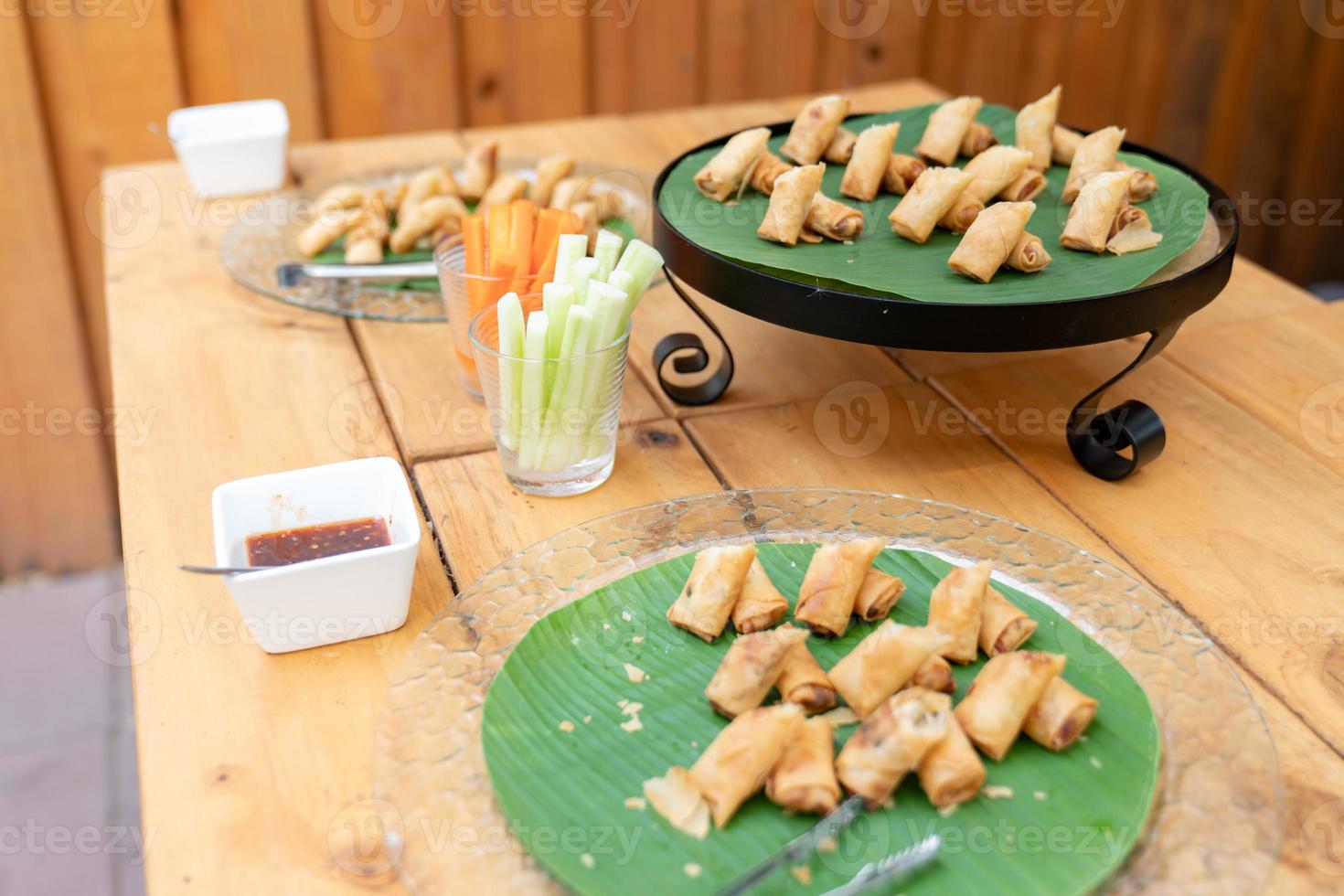 Deep fried spring roll vegetable and vermicelli on circle black plate with banana leaf at an outdoor wood table. photo