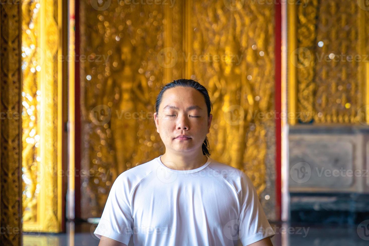 Asian long hair man relaxes meditation with all white costume sit in front of Buddist's gold wallpaper in the Temple, Thailand. photo