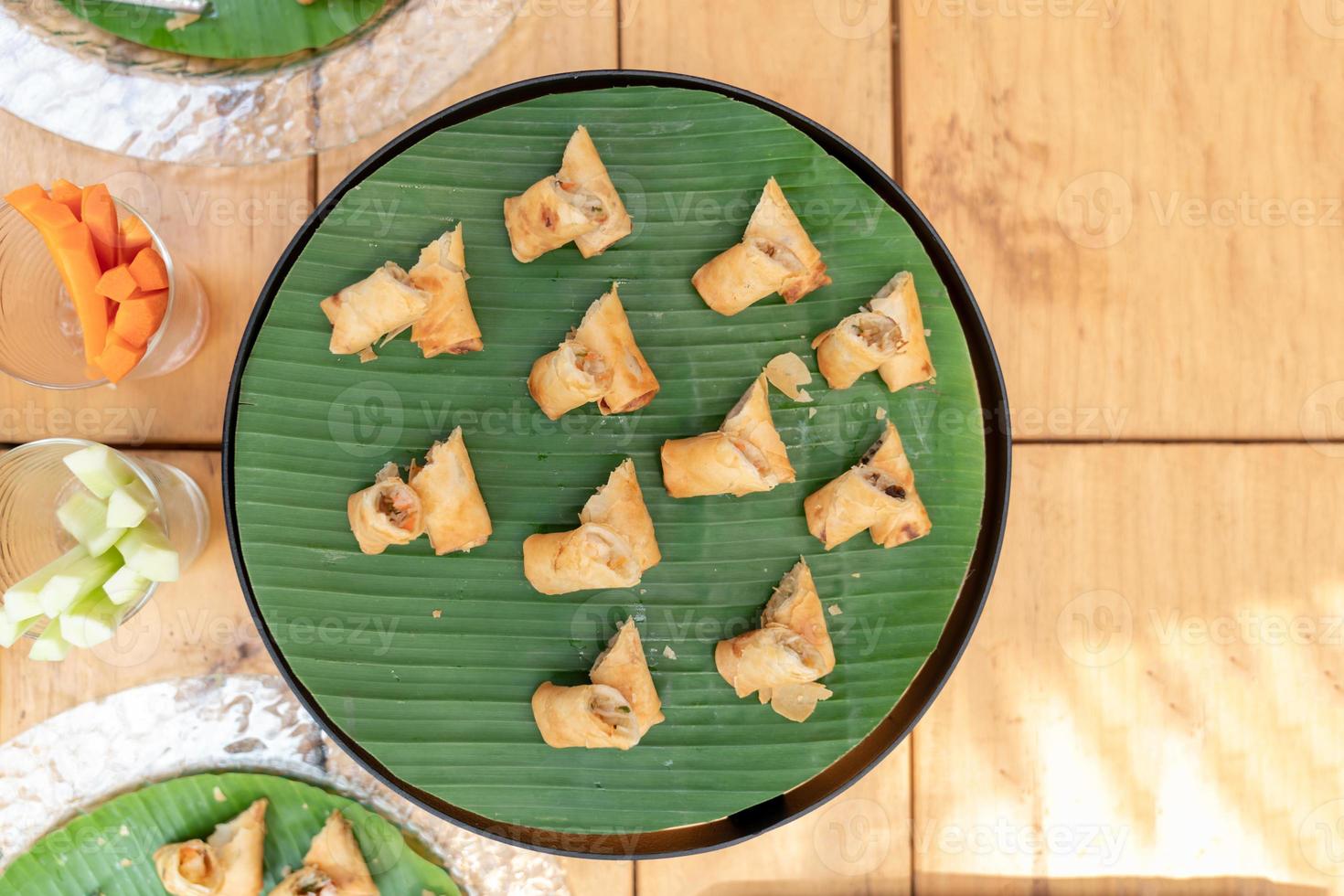 Deep fried spring roll vegetable and vermicelli on circle black plate with banana leaf at an outdoor wood table. photo
