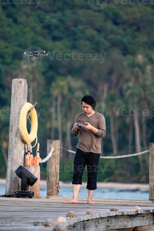 Asian man concentrate to controls and monitors drone on the sea jetty. photo