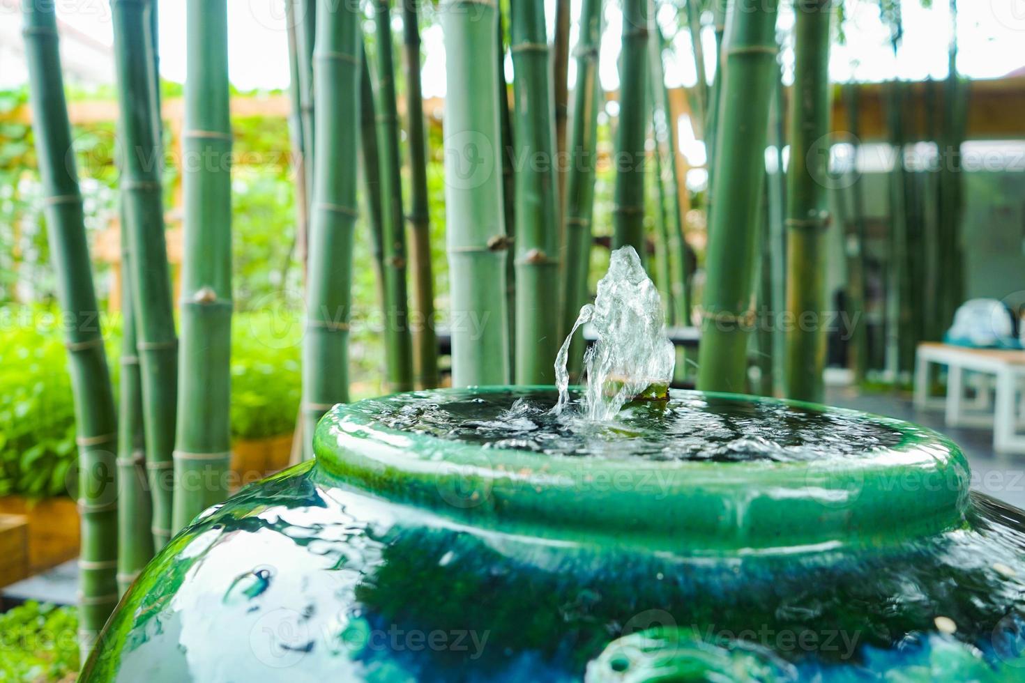 Closeup to little fountain from bamboo stick inside green vintage jar that decorated in the garden with sunlight effect. photo