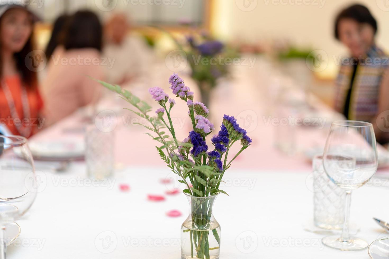 las flores decoran la mesa larga del comedor en el lujoso evento de relajación con la gente social borrosa detrás foto