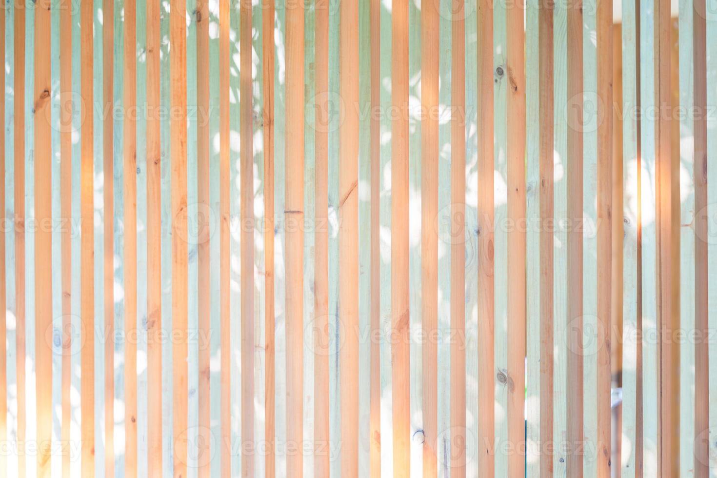 Wood battens in the vertical postion settle on the wall for fence and hording outside of building. It's a background of light from leaf of tree shadow to battens. photo