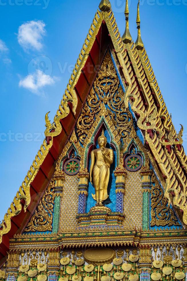 Buddha statue stands on the front of the temple building with beautiful Thai Art pattern style in the open sky day. photo