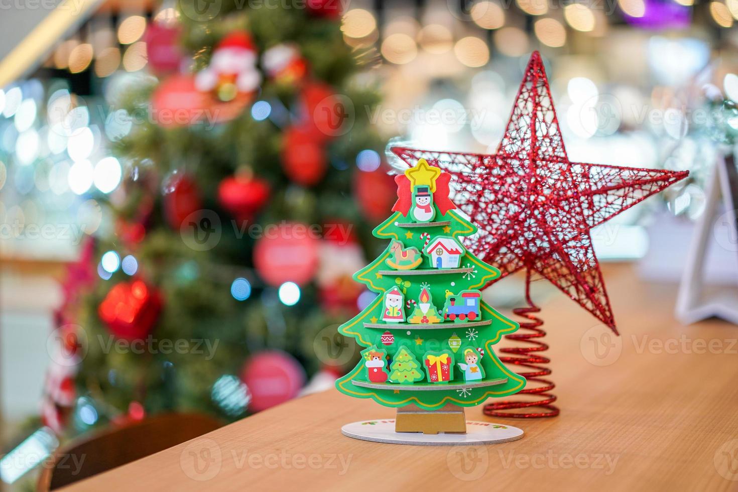 Red star Christmas tree paper craft decoration on the wood table with blur big Christmas tree behide. photo
