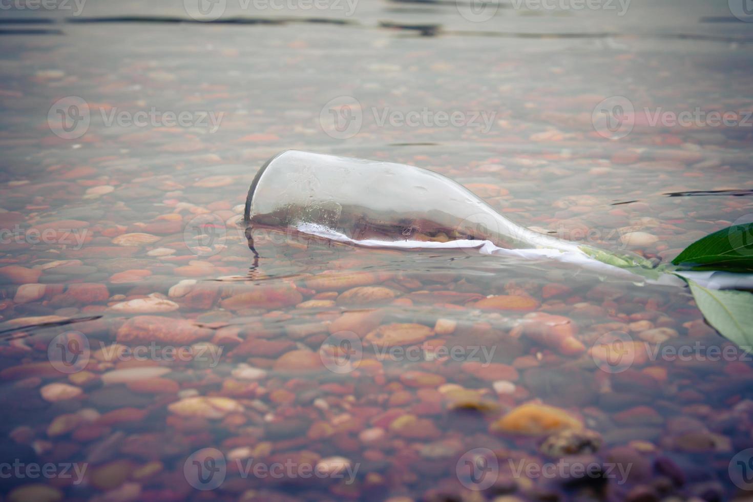 Glass bottle half submerged in a shallow stream photo