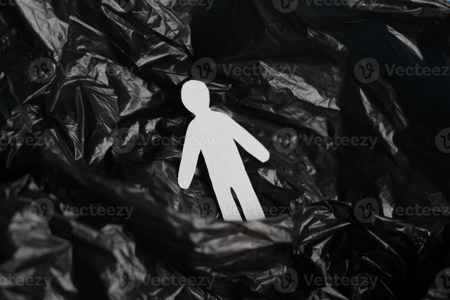 The silhouette of a man carved from white paper is immersed in a black plastic bag. The concept of environmental pollution or mental disorder, loneliness photo