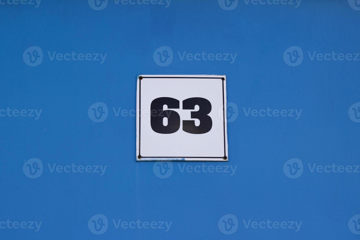 Metal plate with house number 63 black color on white. On a blue wall. The wall of the house photo