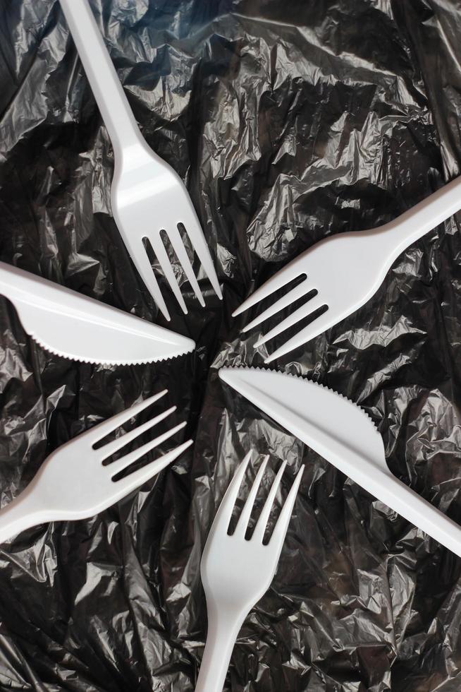 Plastic utensils, white forks and knives on a black plastic bag. Abstract background. Environmental pollution, environmental problems, zero waste, sustainable living photo