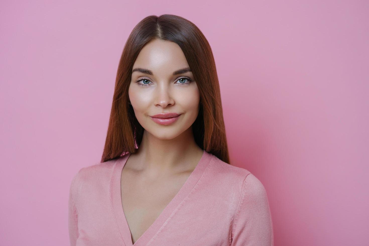 Portrait of good looking young European woman with long hair, has well cared complexion, dressed in casual clothes, isolated over pink background. People, face expressions and beauty concept. photo