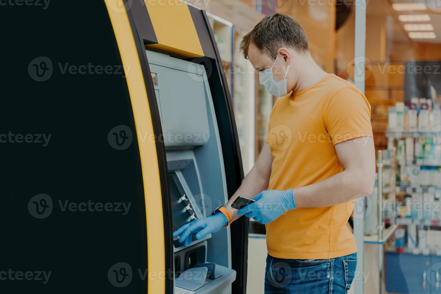 Man wears protective mask and medical gloves, uses ATM machine, prevents from virus pandemic, introduces pin code. Safe money withdrawal during coronavirus outbreak. Payment, influenza concept photo