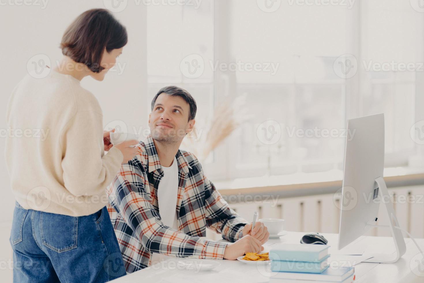 Family, paper work and technology concept. Husband and wife study contract agreement, read terms and conditions, discuss domestic bills, drinks coffee, man poses at desktop with modern computer photo