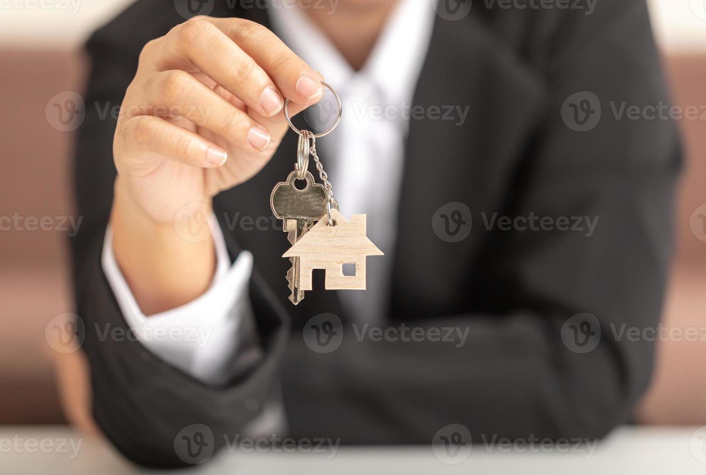 Hand of a woman holding a wooden model house and a key showing to the front. photo