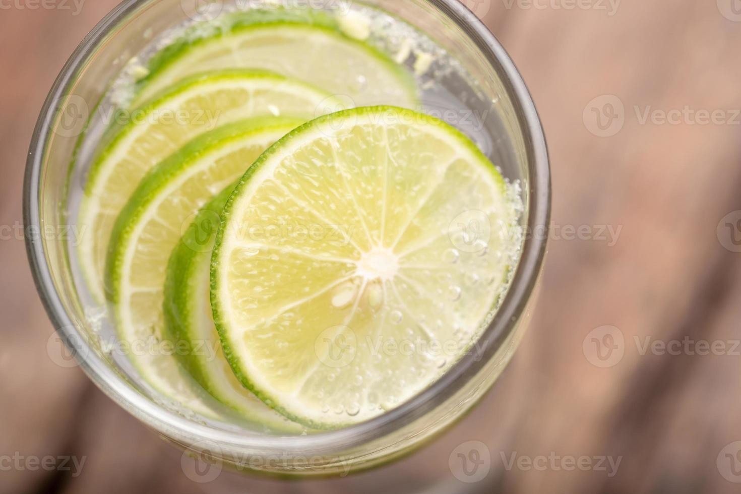 Close up top view green lime sliced in the soda water and glass place on the wooden table with blurred background photo