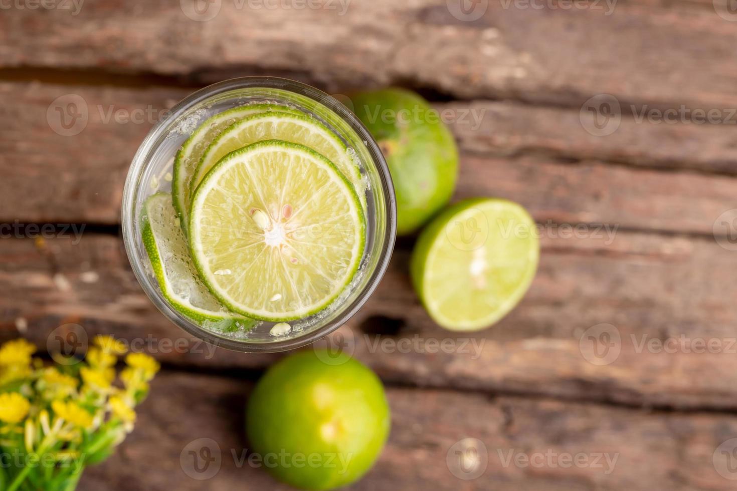 Top view green lime sliced in the soda water and glass place on the wooden table with yellow flowers photo