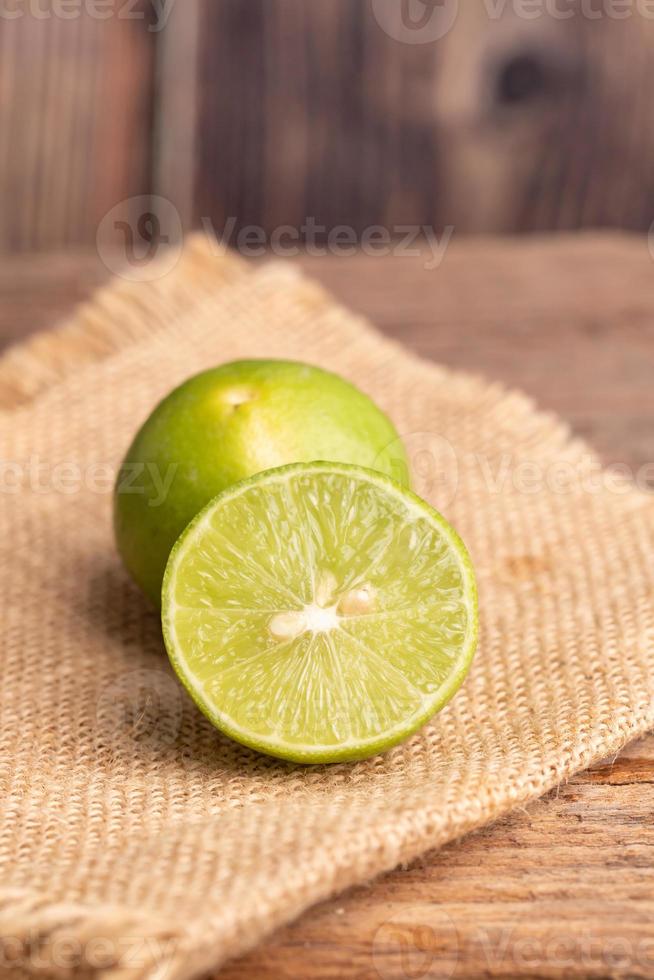 Close up a half of the green lime and seed place on woven sack on the wooden table in a kitchen photo
