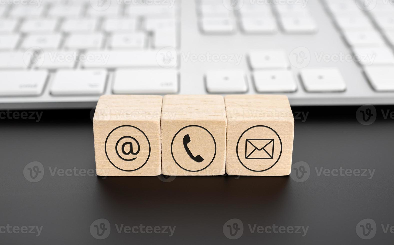 Contact us icons on wooden blocks and computer keyboard on black desk photo
