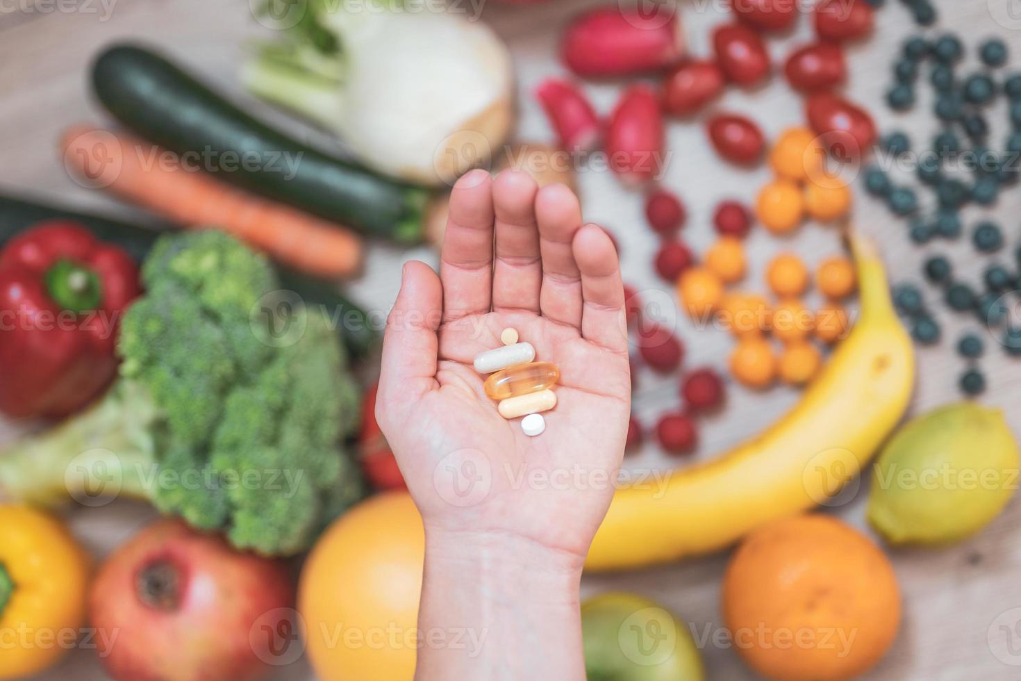 mano sujetando suplementos alimenticios sobre verduras y frutas para un estilo de vida saludable foto