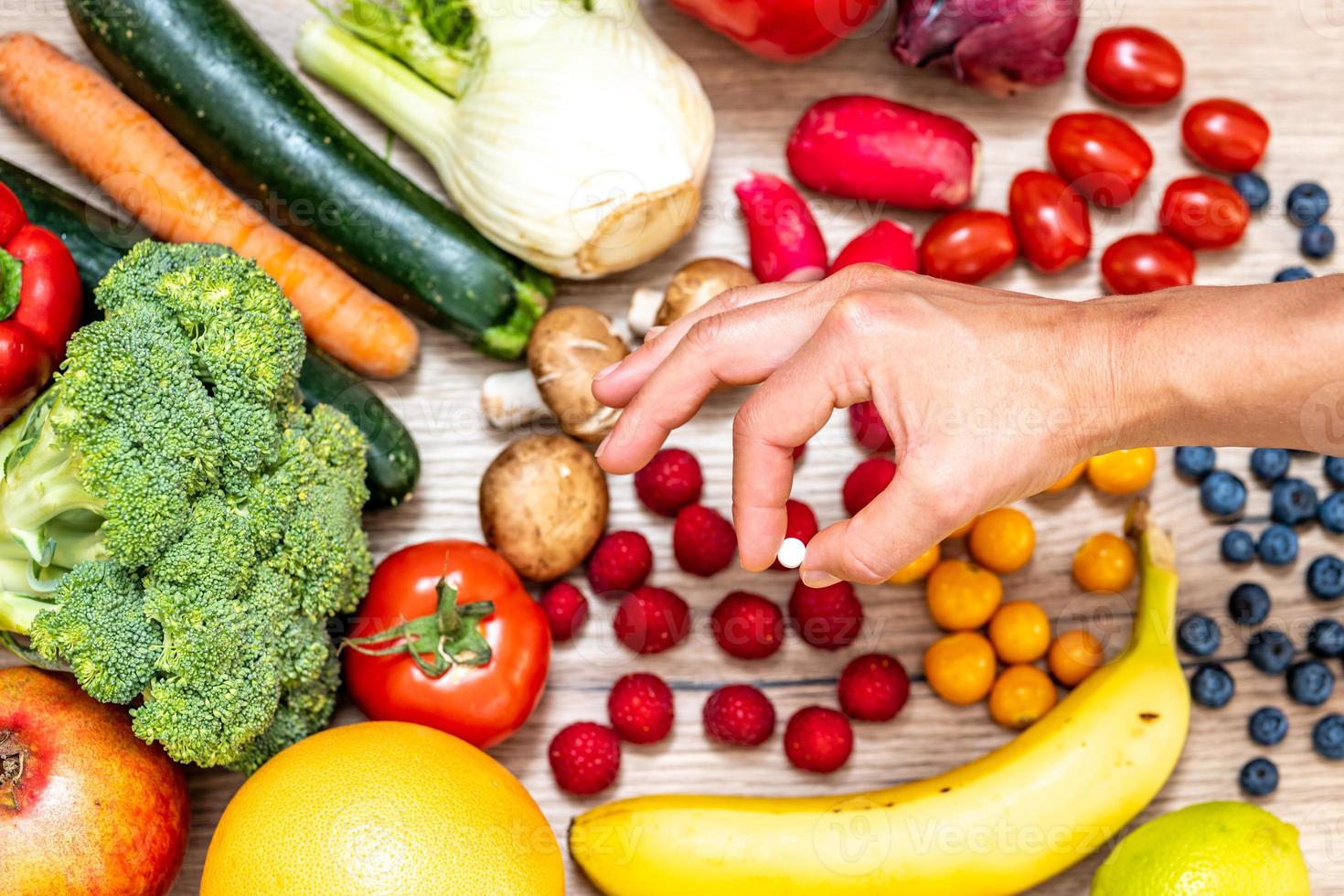 Hand holding food supplements over vegetables and fruits for a healty lifestyle photo