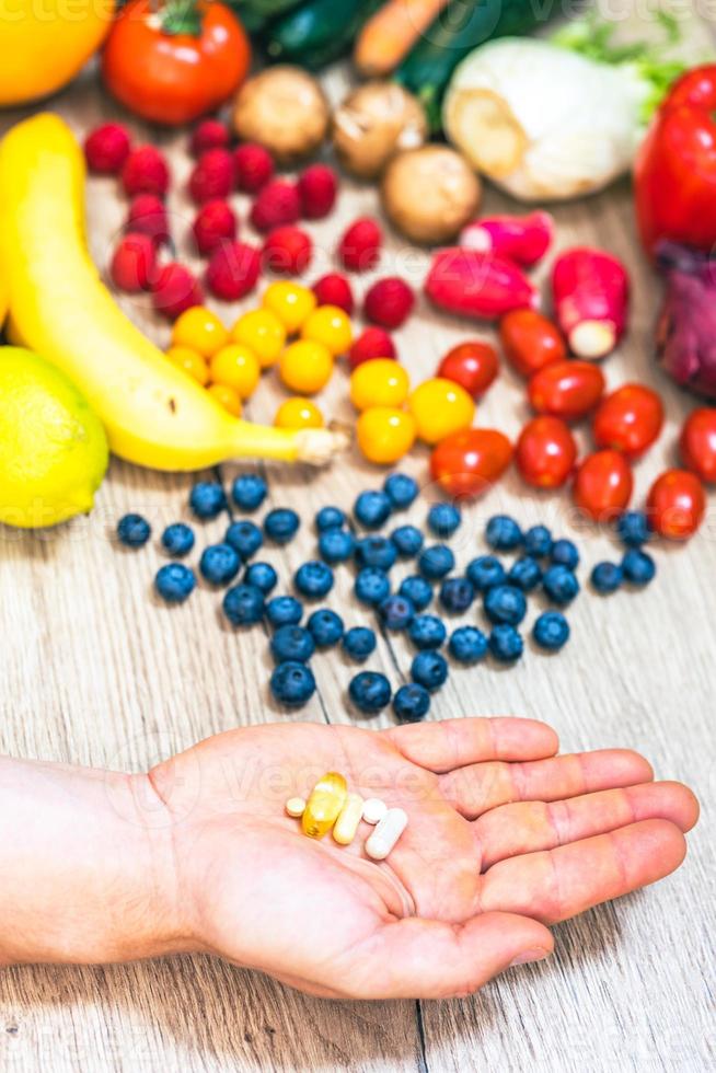 Hand holding food supplements over vegetables and fruits for a healty lifestyle photo