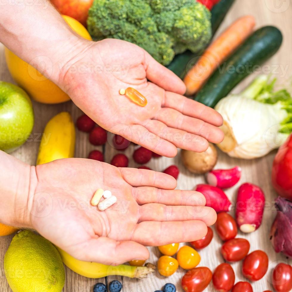 mano sujetando suplementos alimenticios sobre verduras y frutas para un estilo de vida saludable foto