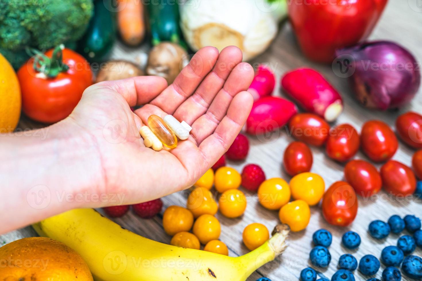 mano sujetando suplementos alimenticios sobre verduras y frutas para un estilo de vida saludable foto